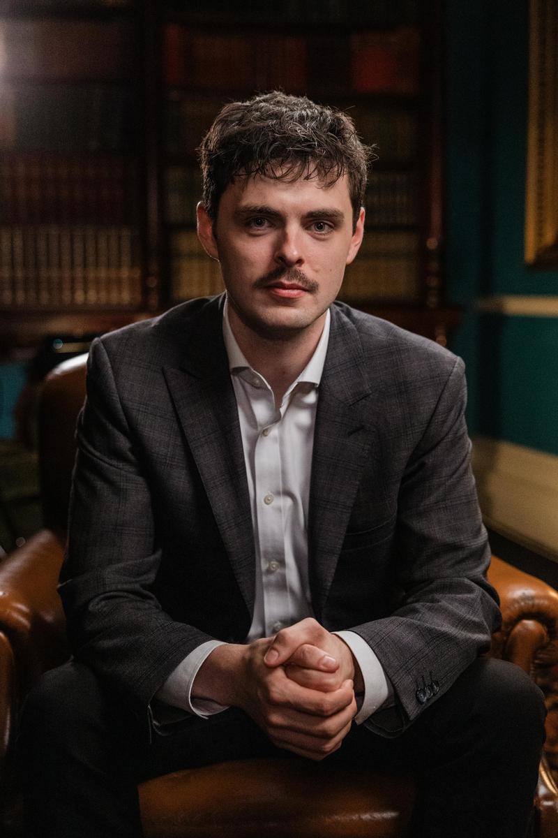 Alex O'Connor sat in a suit with library background