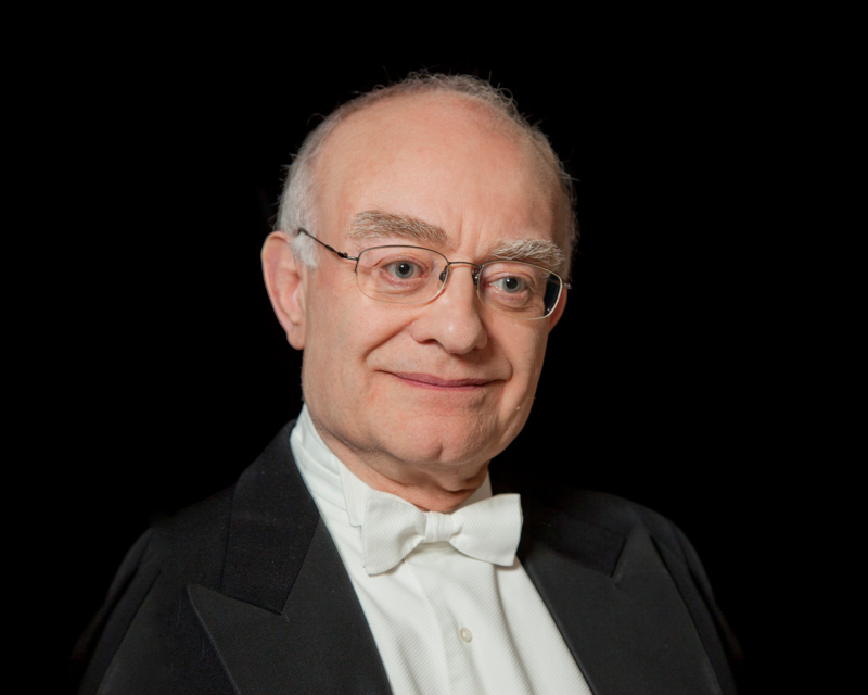 An older man smiles at the camera in a suit with a white bow tie.