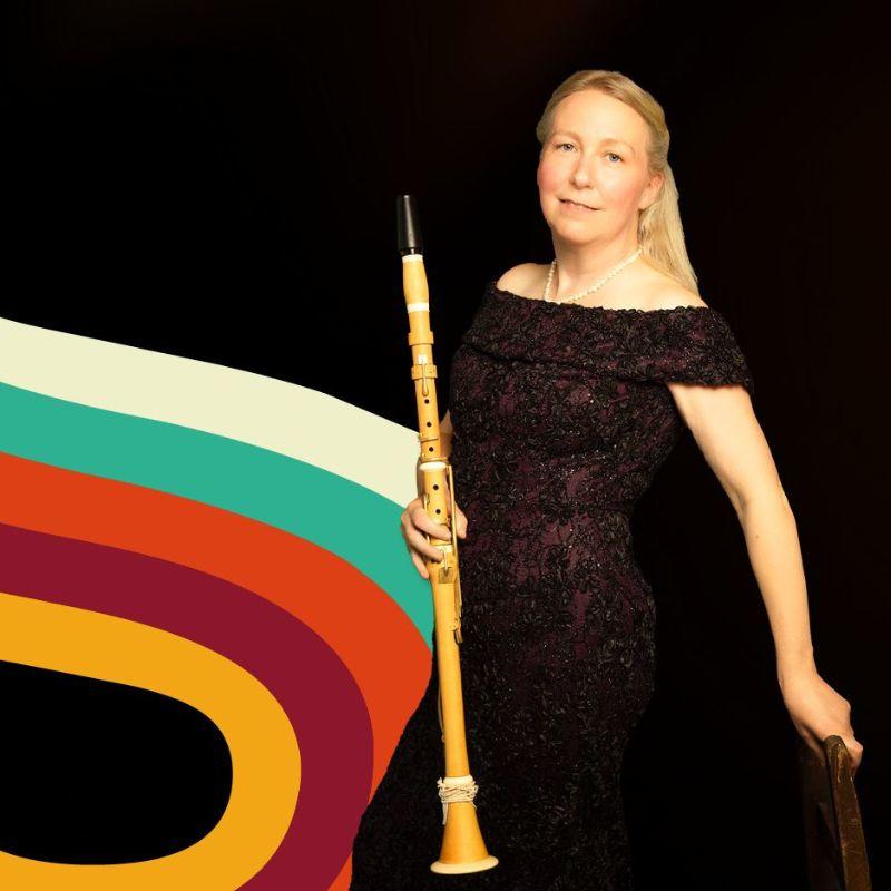 A musician stands in a sparkling black gown leaning against the back of a chair, her hair loose down her back.