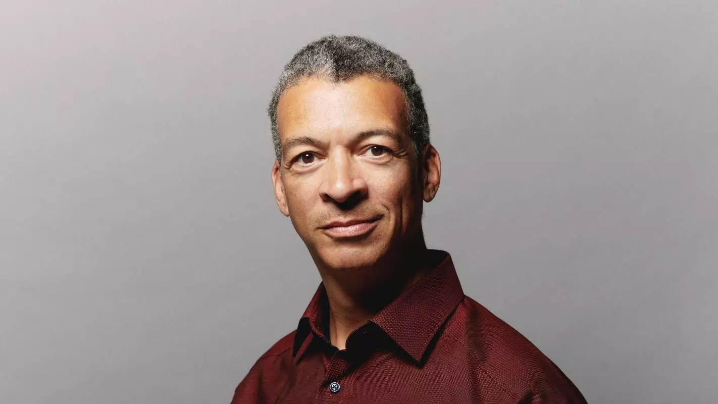 Man in burgundy shirt with neutral expression looking towards the camera