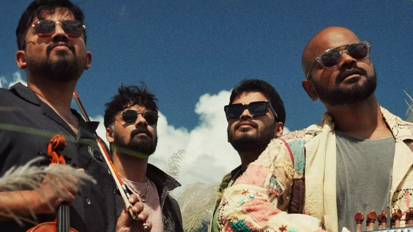 Four men in sunglasses looking into camera with a blue sky with clouds behind them