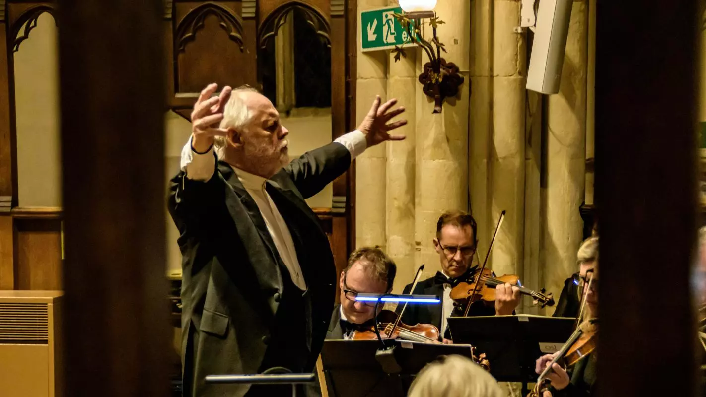 Conductor in a suit with his arms open to an orchestra